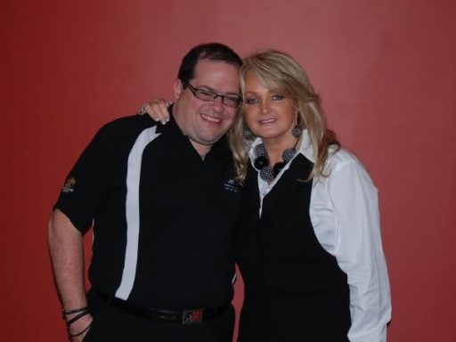 Two people posing together, smiling against a red background.