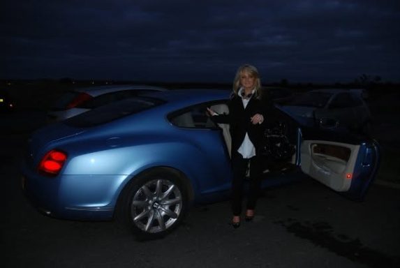 A person standing next to a blue car with the door open, under a dark sky.